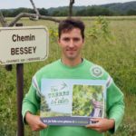 Guillaume Robin avec le panneau « Ici, je fais une place à la nature », devant un perchoir à rapaces improvisé avec une branche © LPO Drôme